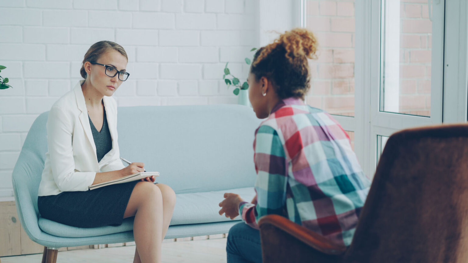 Therapist taking notes during a counselling session with a client in a bright consulting room