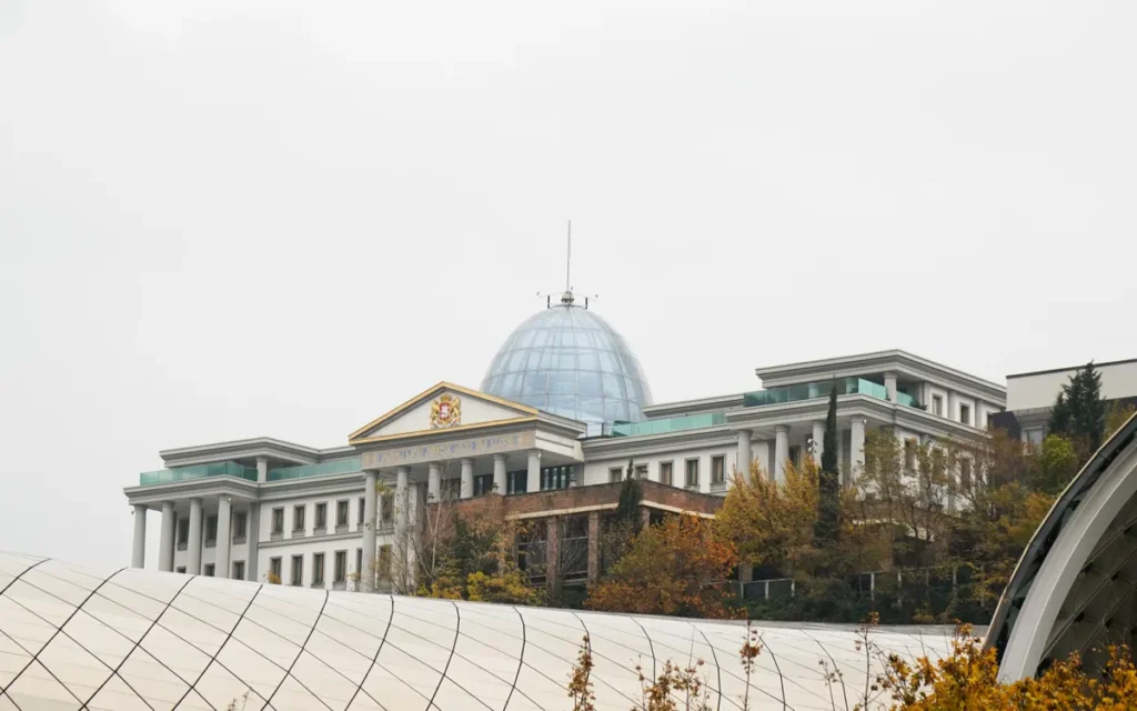 A modern palace with a dome surrounded by autumn trees under an overcast sky